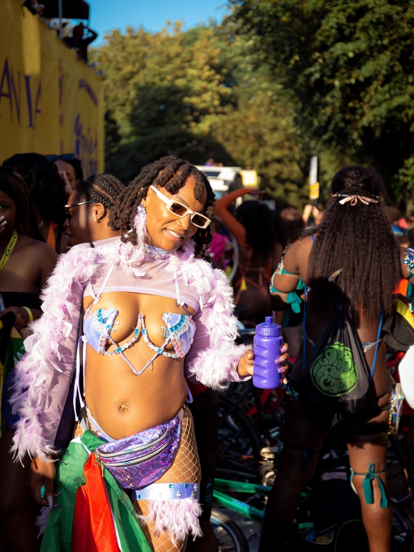 A Woman In A Feathered Purple Carnival Outfit And Sunglasses Posing During A Parade.